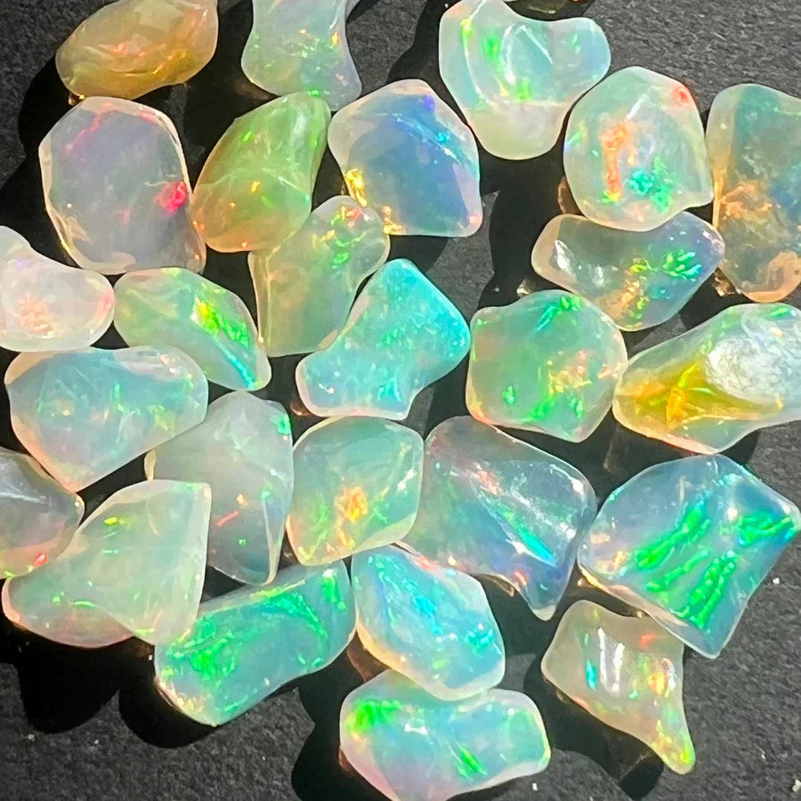 Cristale naturale de opal în nuanțe de alb, albastru, negru și portocaliu, simbol al viselor, transformării interioare și echilibrului emoțional.